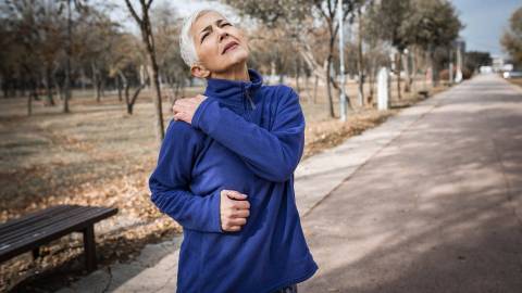 A gray-haired woman out for a run: she is grabbing her right shoulder with her left hand as it is obviously extremely painful.