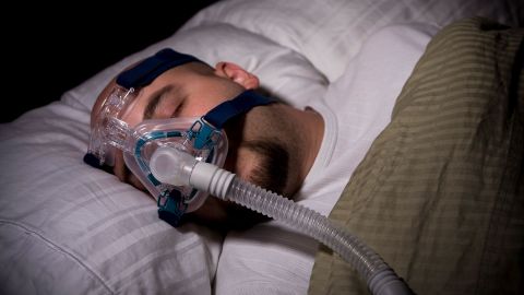 Sleep apnea: man lying in bed wearing a respiratory mask. He appears to be asleep.