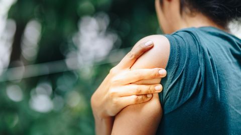 Schulterschmerzen: Eine Frau fasst sich mit ihrer rechten Hand an die schmerzende Schulter.