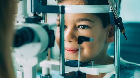 Amblyopia in children: boy sitting in front of a slit lamp in an ophthalmology clinic treatment room having a visual acuity test.