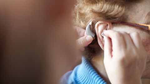 Hearing impairment and hearing loss: man fitting a hearing device in an older woman’s ear.