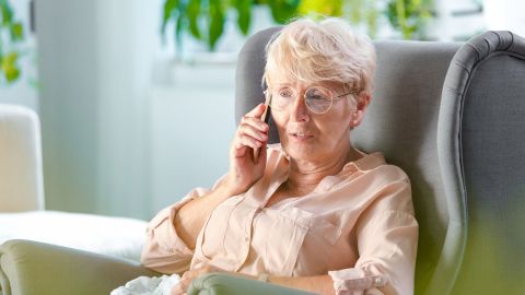 Eine Frau mittleren Alters lehnt in einem großen Sessel. Mit der rechten Hand hält sie sich ein mobiles Telefon ans Ohr.