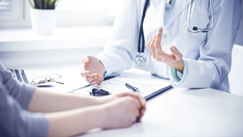 Doctor and patient sitting at a table. Having a conversation. The patient is obtaining a second opinion. A printout from a health record is on the table in front of the doctor.