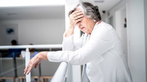 Tension headaches: older woman leaning on a rail clutching her forehead with one hand. The woman looks exhausted.