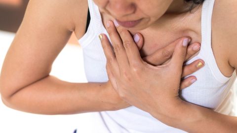 Speiseröhrenkrebs: Eine Frau fasst sich mit beiden Händen an den oberen Brustkorb. Sie wirkt angespannt, als hätte sie Schmerzen.