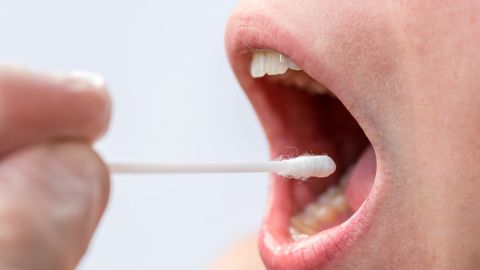 Cotton bud being introduced into a person’s open mouth.