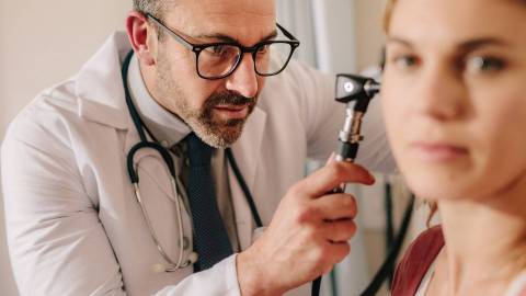 Arzt untersucht Ohr einer Patientin mit Otoskop