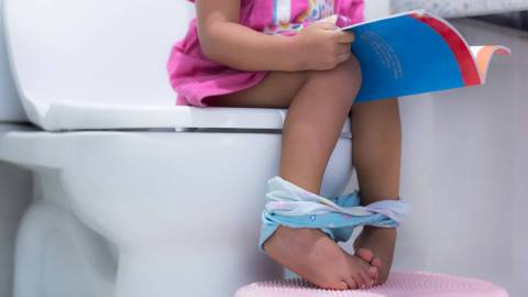 Ein kleines Kind sitzt auf der Toilette. Seine Füße stehen auf einem Höckerchen.