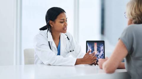 A patient is talking with her doctor. A monitor shows a section of the spine.