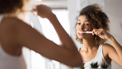 Genç bir kadın dişlerini fırçalıyor ve aynada kendine bakıyor.
