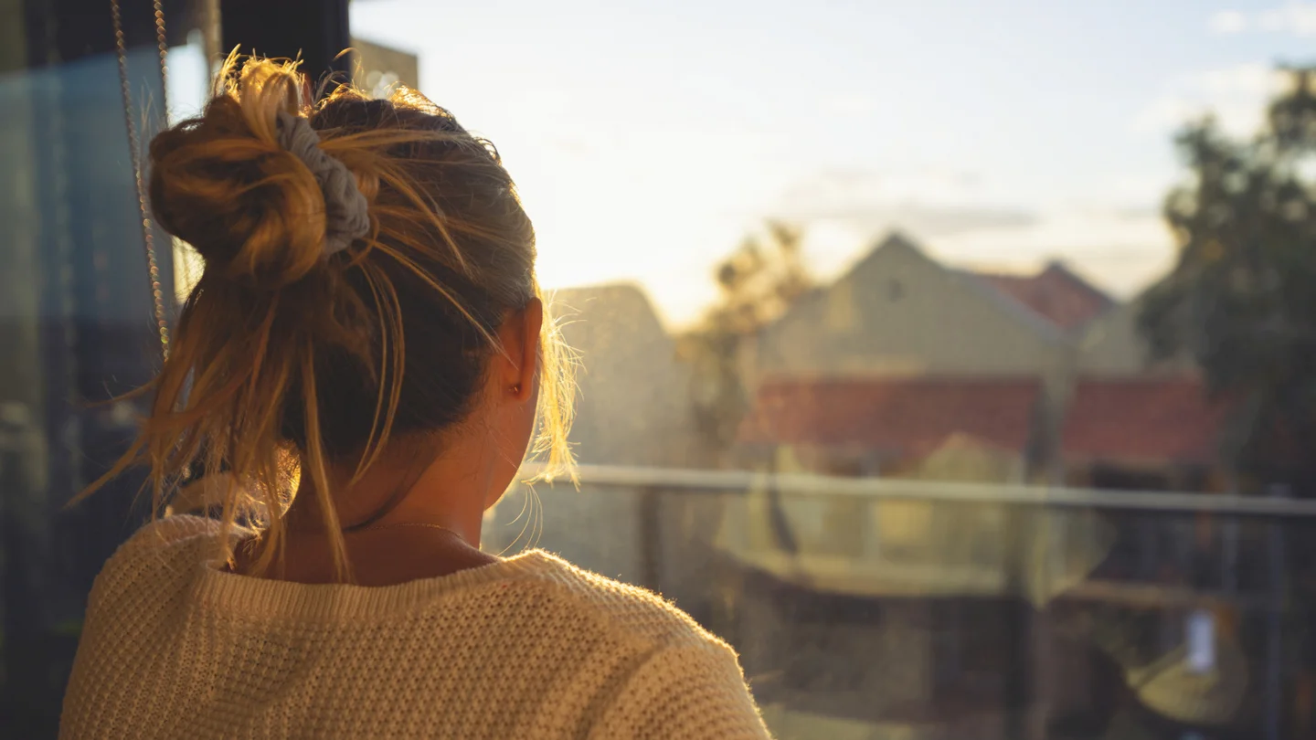 Eine junge Frau schaut bei Sonnenuntergang durch das Fenster.