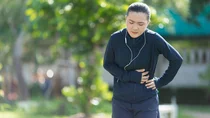 Eine junge Frau in Joggingkleidung ist draußen stehengeblieben und hält sich die linke Bauchseite.