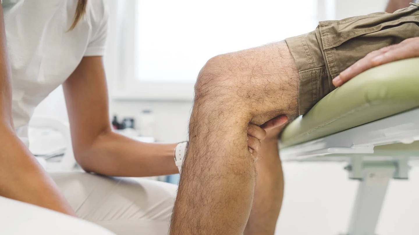 Eine &Auml;rztin untersucht die Kniekehle eines Patienten.