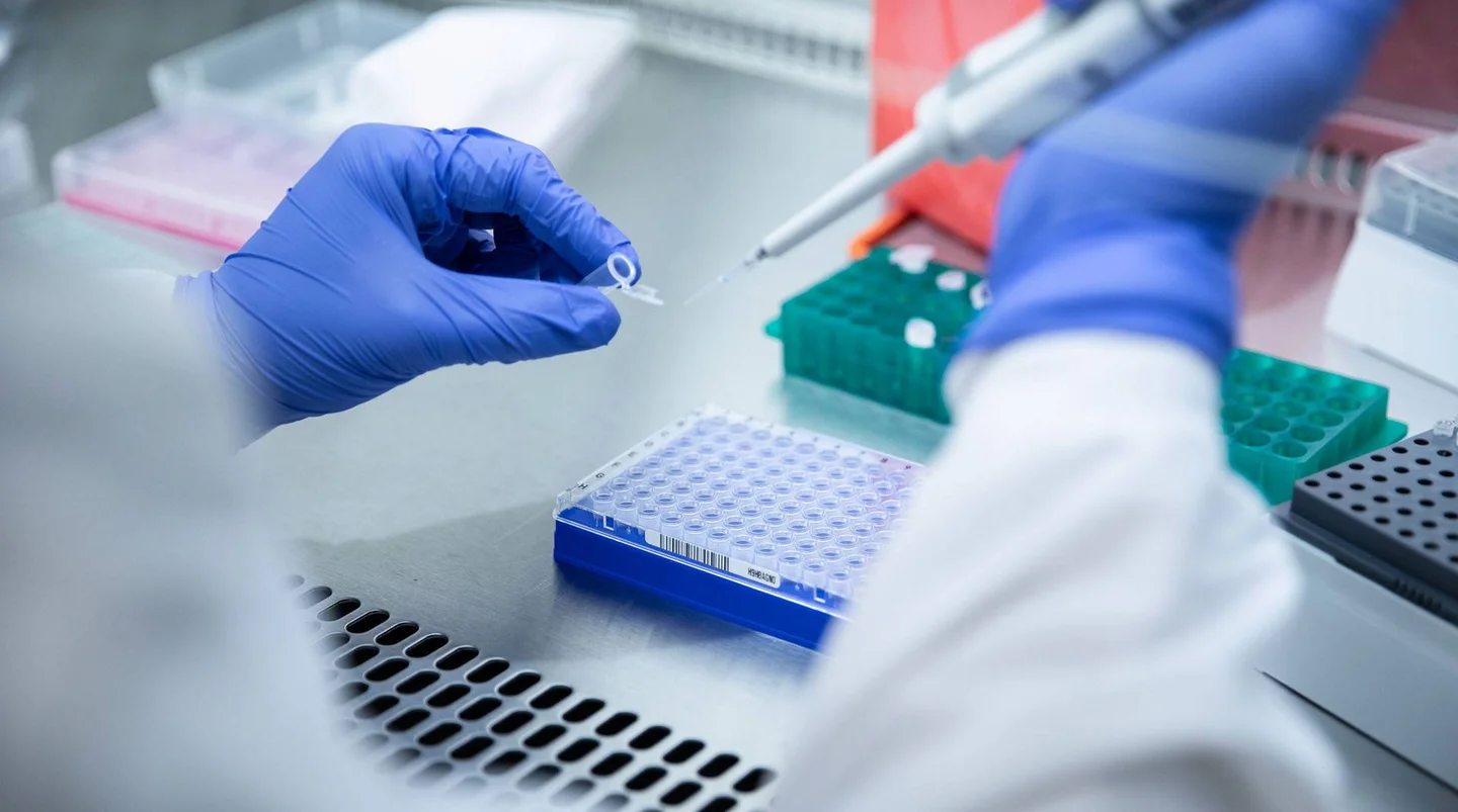Laborarbeit: Person in Schutzkleidung und Handschuhen mit Pipette und Probenröhrchen