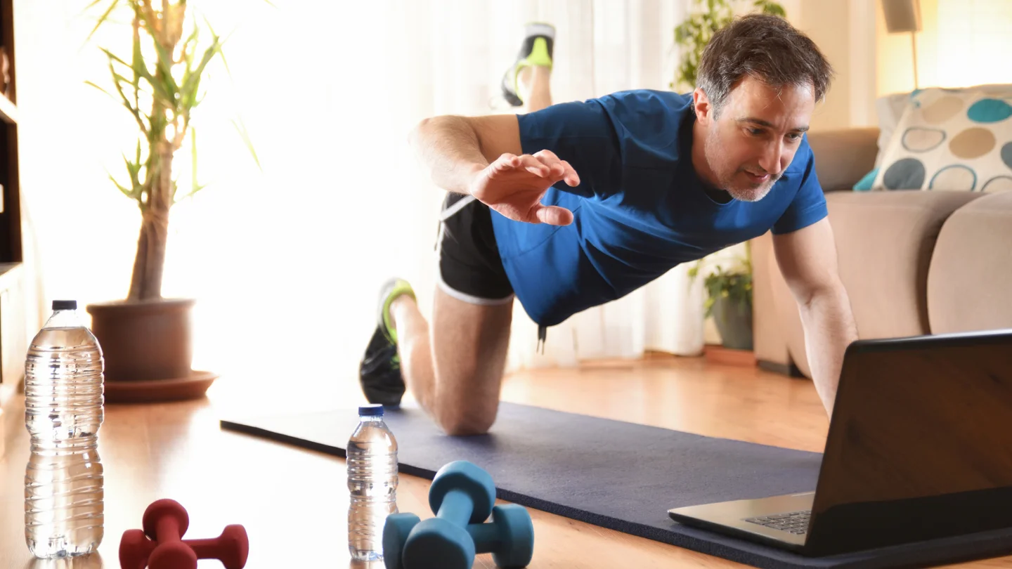 Ein Mann macht auf der Yogamatte &Uuml;bungen vor seinem Laptop.