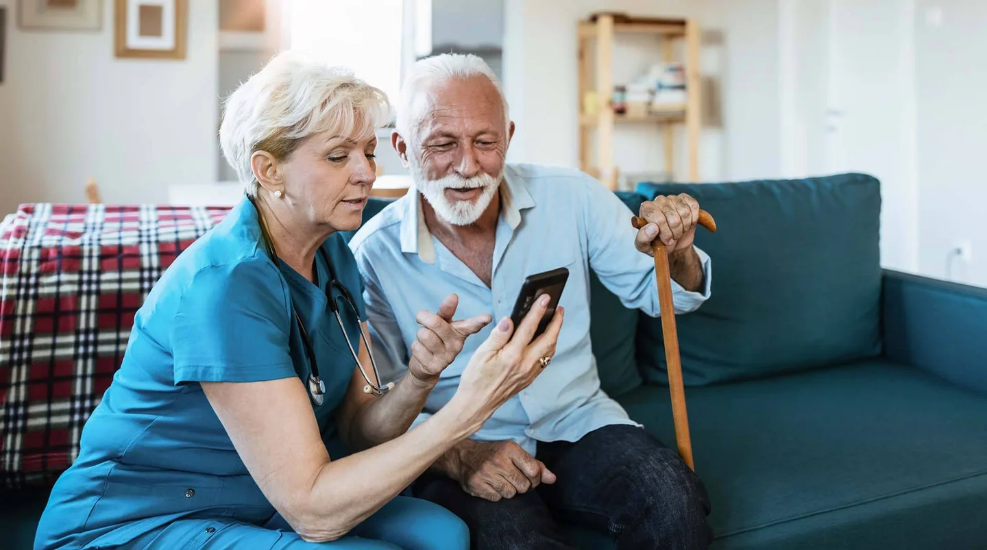 Pflegerin zeigt älterem Mann etwas auf dem Smartphone.