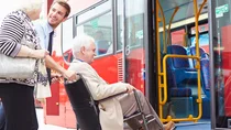 Ein junger Busfahrer schiebt einen älteren Herrn im Rollstuhl über eine Rampe in den Bus.
