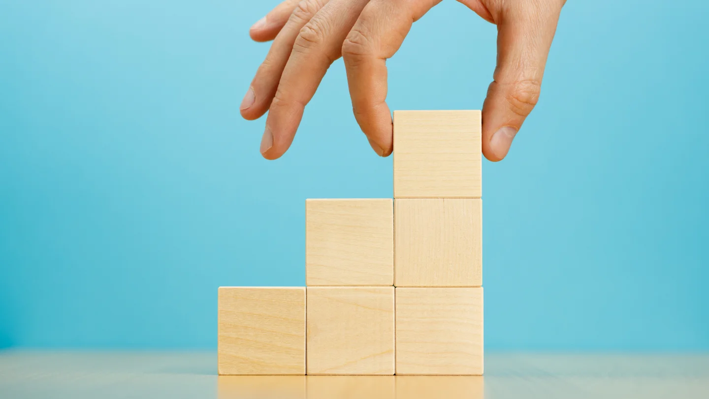 Eine Person setzt mit der Hand mehrere W&uuml;rfel zu einer Treppe zusammen.