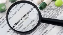 Ausschnitt eines Beipackzettels, auf dem einige Tabletten liegen. Der Satz „Welche Nebenwirkungen sind möglich?“ wird unter einer Lupe vergrößert.