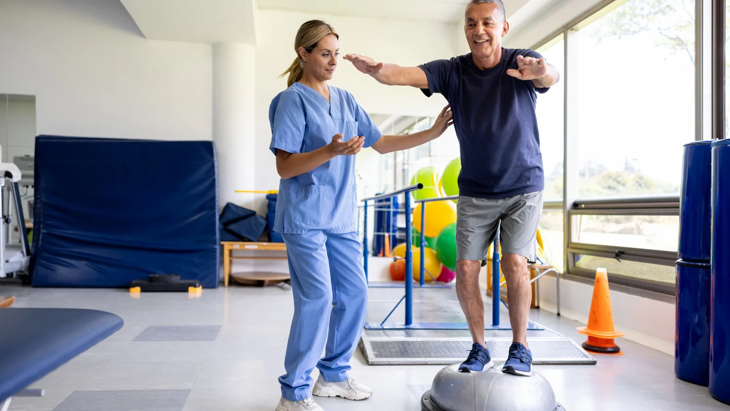 Ergotherapeutin und Patient trainieren das Gleichgewicht auf einem wackeligen Untergrund.