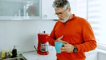 Ein Mann mit Gastritis hält eine Kaffeetasse in der Hand und fasst sich an den schmerzenden Bauch.