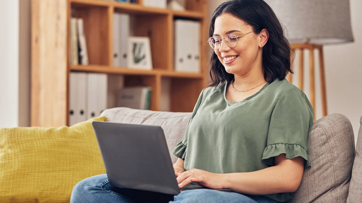 Eine junge Frau sitzt mit einem Laptop auf einem Sofa.