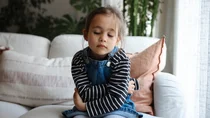Kind sitzt mit Bauchschmerzen auf dem Sofa.