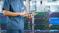 Eine medizinische Fachkraft bedient ein Tablet, im Hintergrund sind Monitore zur Kreislauf&uuml;berwachung sichtbar.